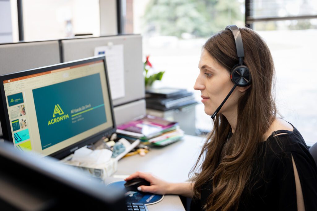 Woman on headset working at a desk with Acronym on computer